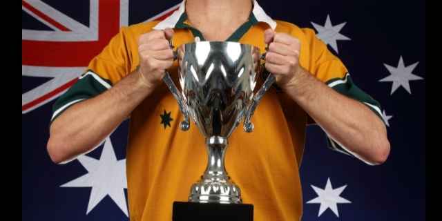 player in australian shirt holding a cup in front of an australian flag
